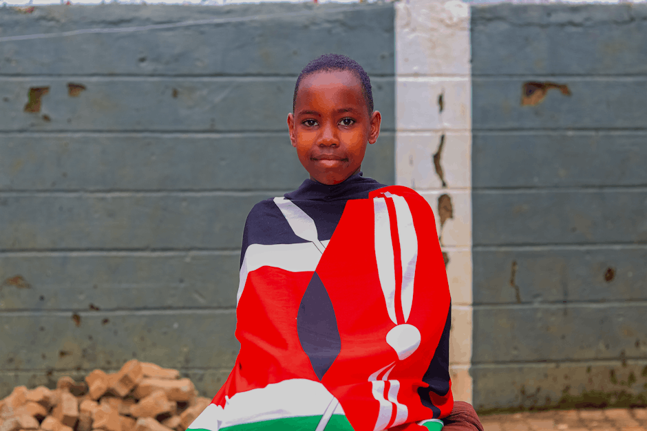A young Kenyan girl proudly wrapped in the national flag, showcasing cultural pride outdoors.